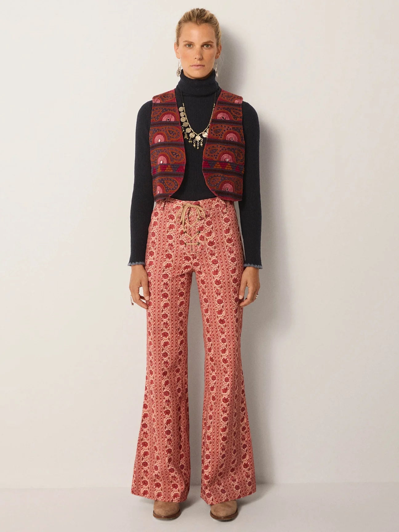 Person wearing a patterned vest, black turtleneck, and pink floral patterned pants 