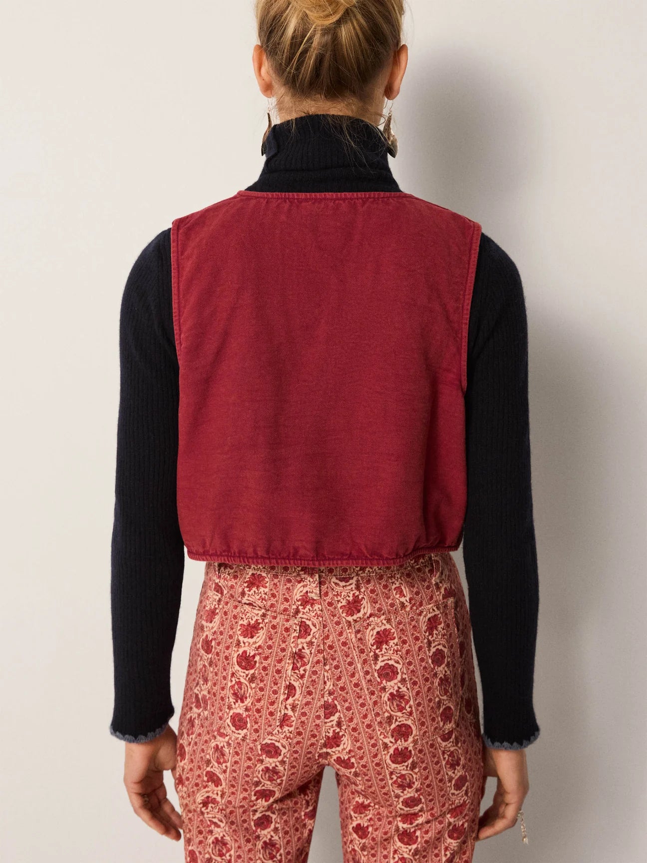 A woman wearing a red vest over a black shirt with patterned pants from Maison Hotel