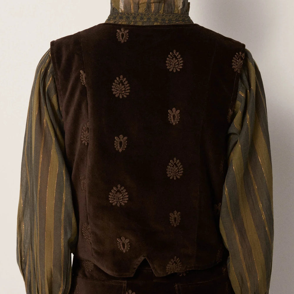 A woman wearing a dark brown vest with tonal embroidery over a green blouse