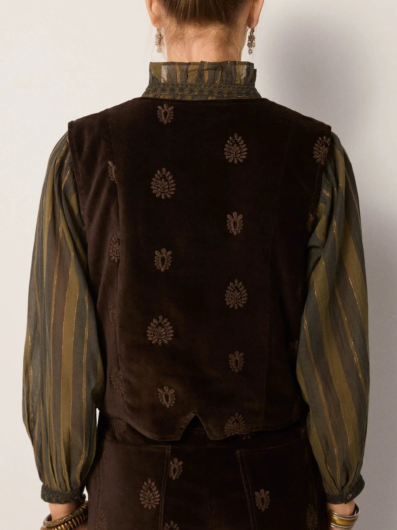 A woman wearing a dark brown vest with tonal embroidery over a green blouse