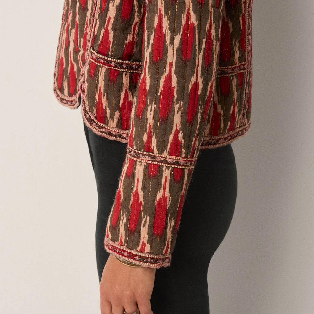 
                      
                        Person wearing a patterned jacket with an artful red and brown design and embroidery along the piping
                      
                    
