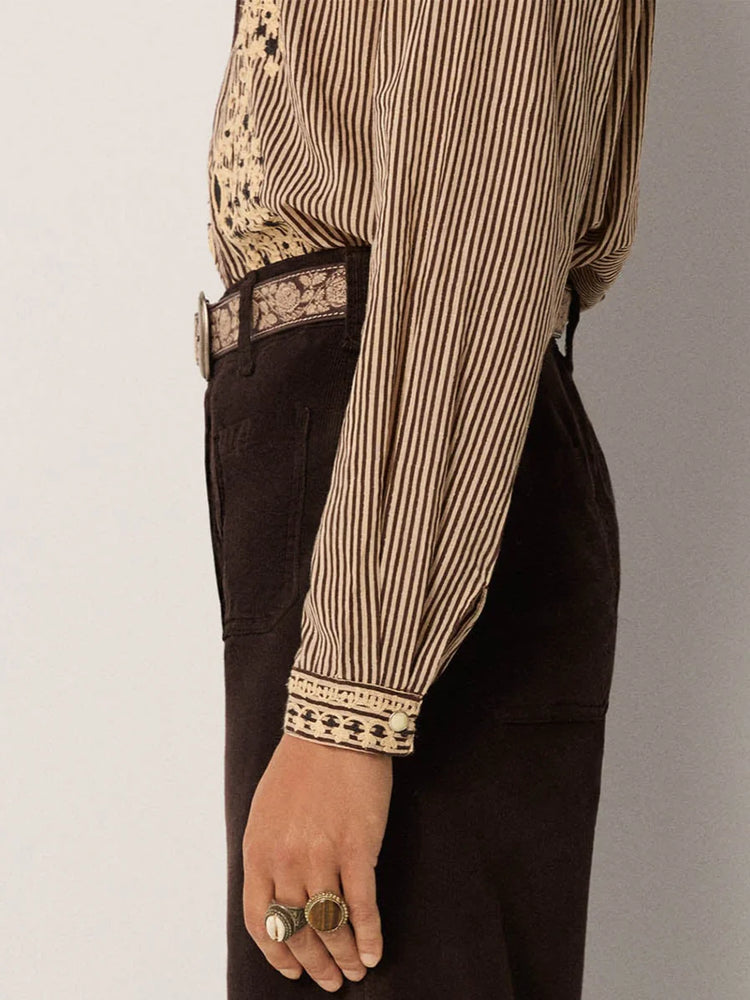 
                      
                        Person wearing a striped shirt with intricate patterns and dark pants 
                      
                    