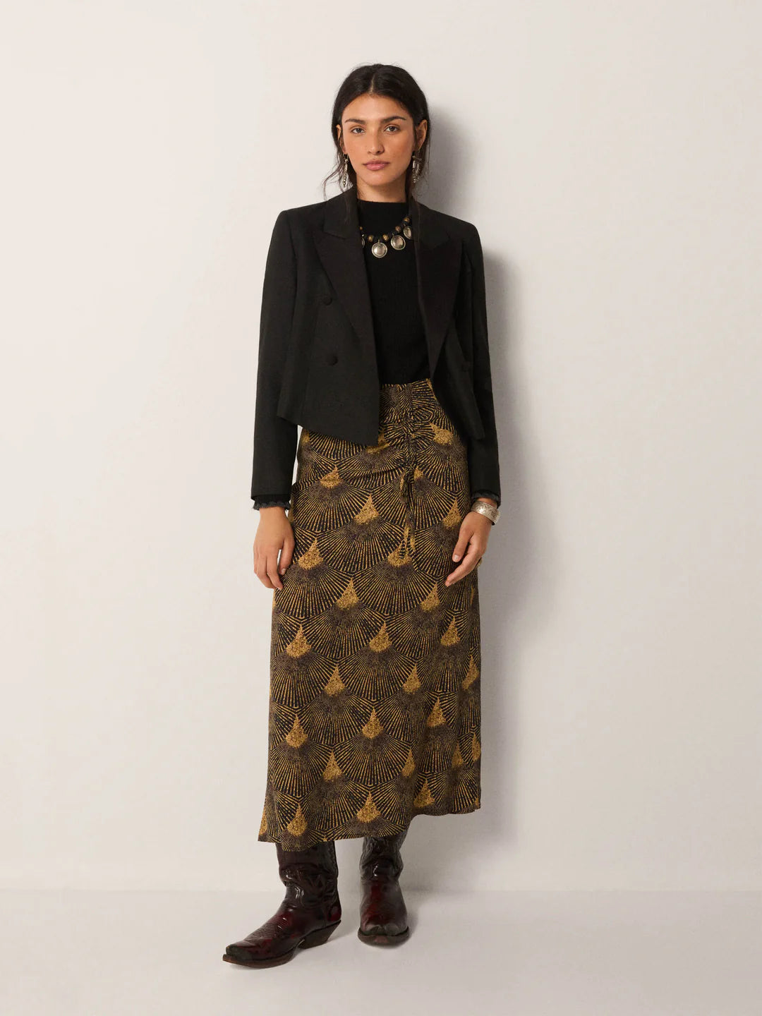 Woman wearing a black blazer, black top, and the Maison Hotel Peacok Avocado Lala Skirt