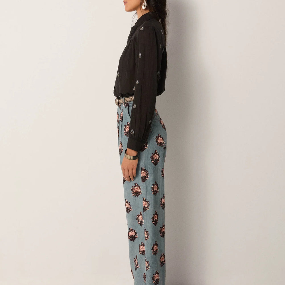 A woman wearing light blue wide leg trousers with rose medallion details