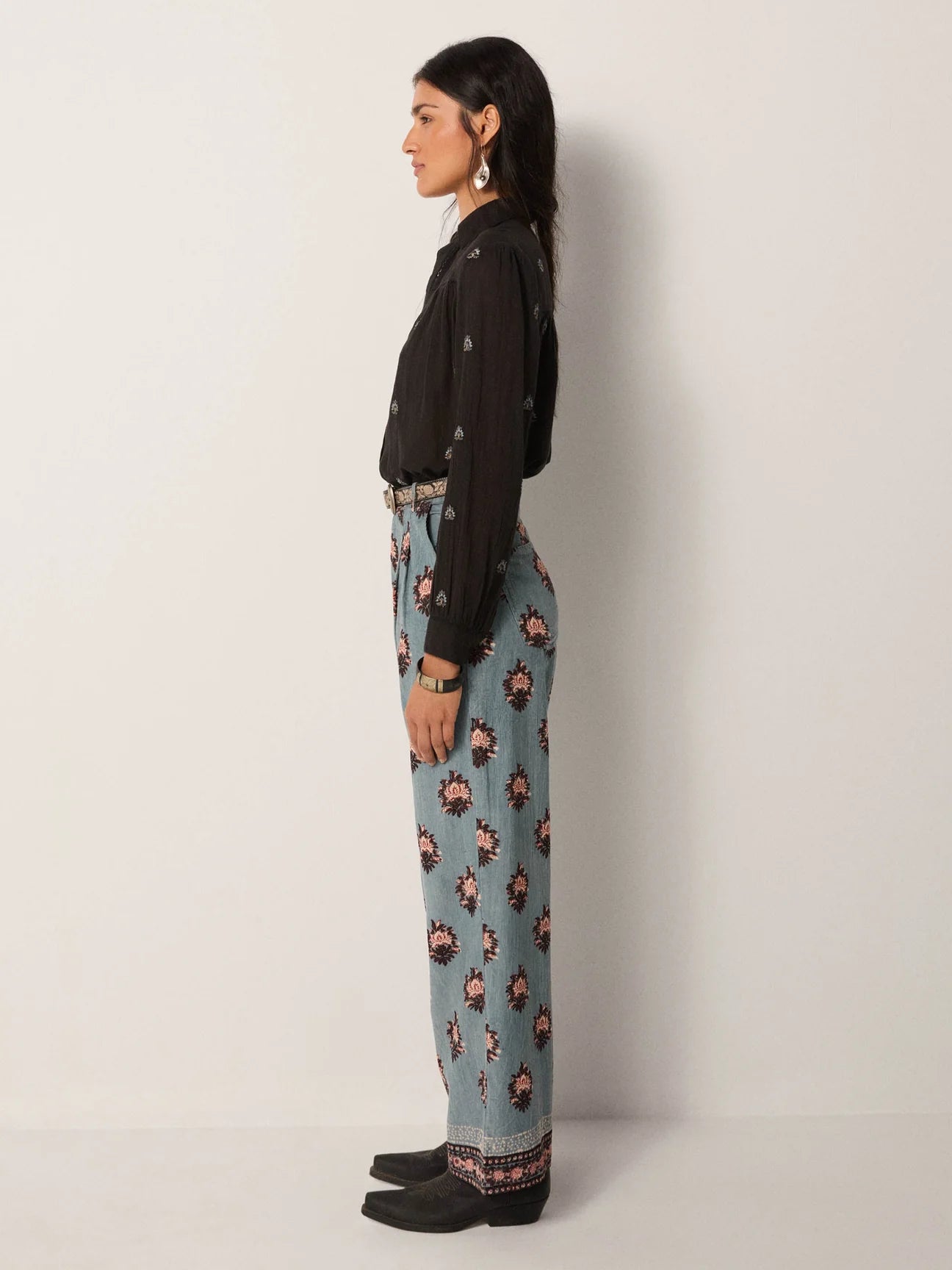 A woman wearing light blue wide leg trousers with rose medallion details