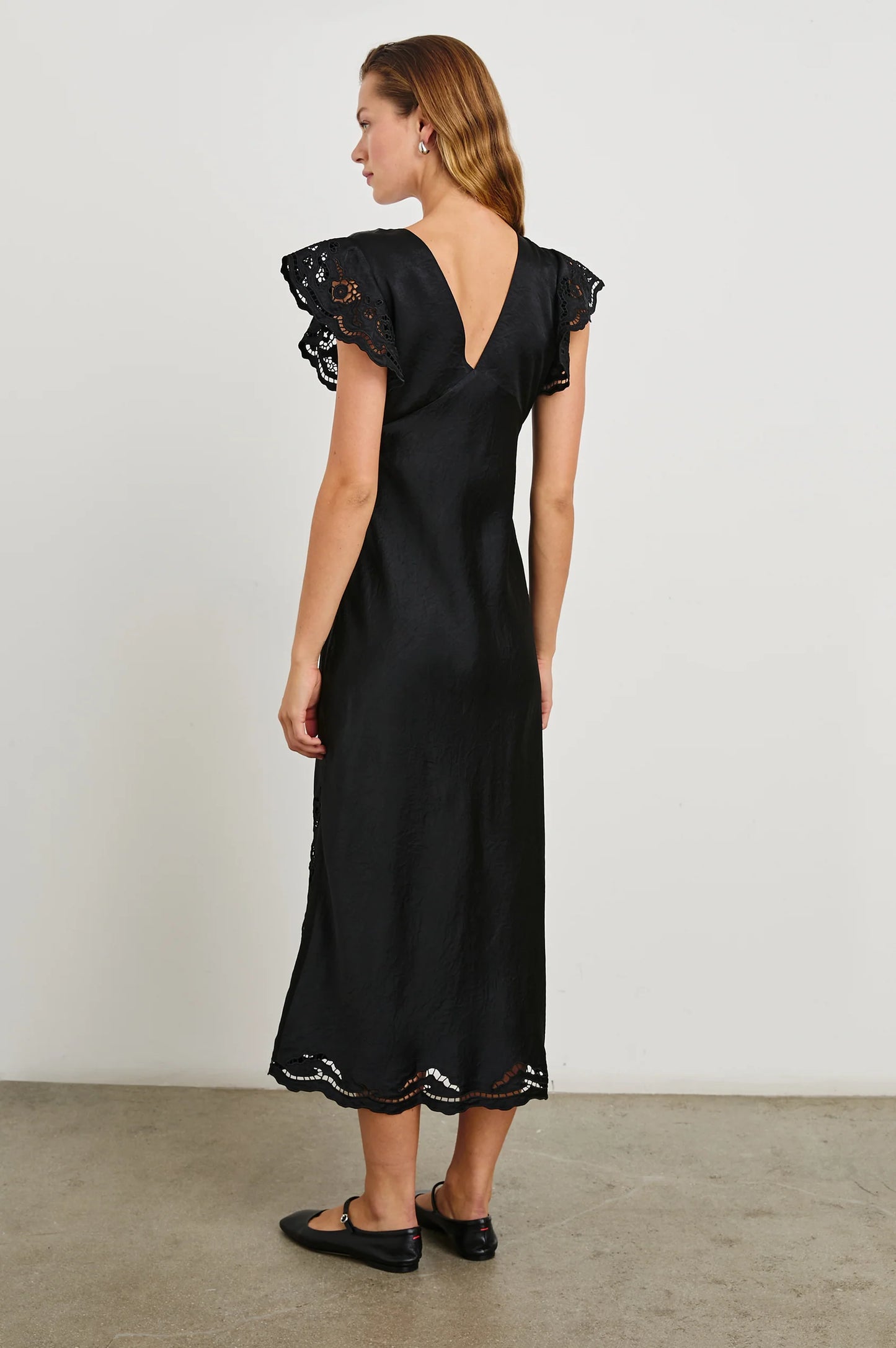 Back view of a woman wearing the Black Eyelet McKenna Satin Midi Dress by the brand Rails