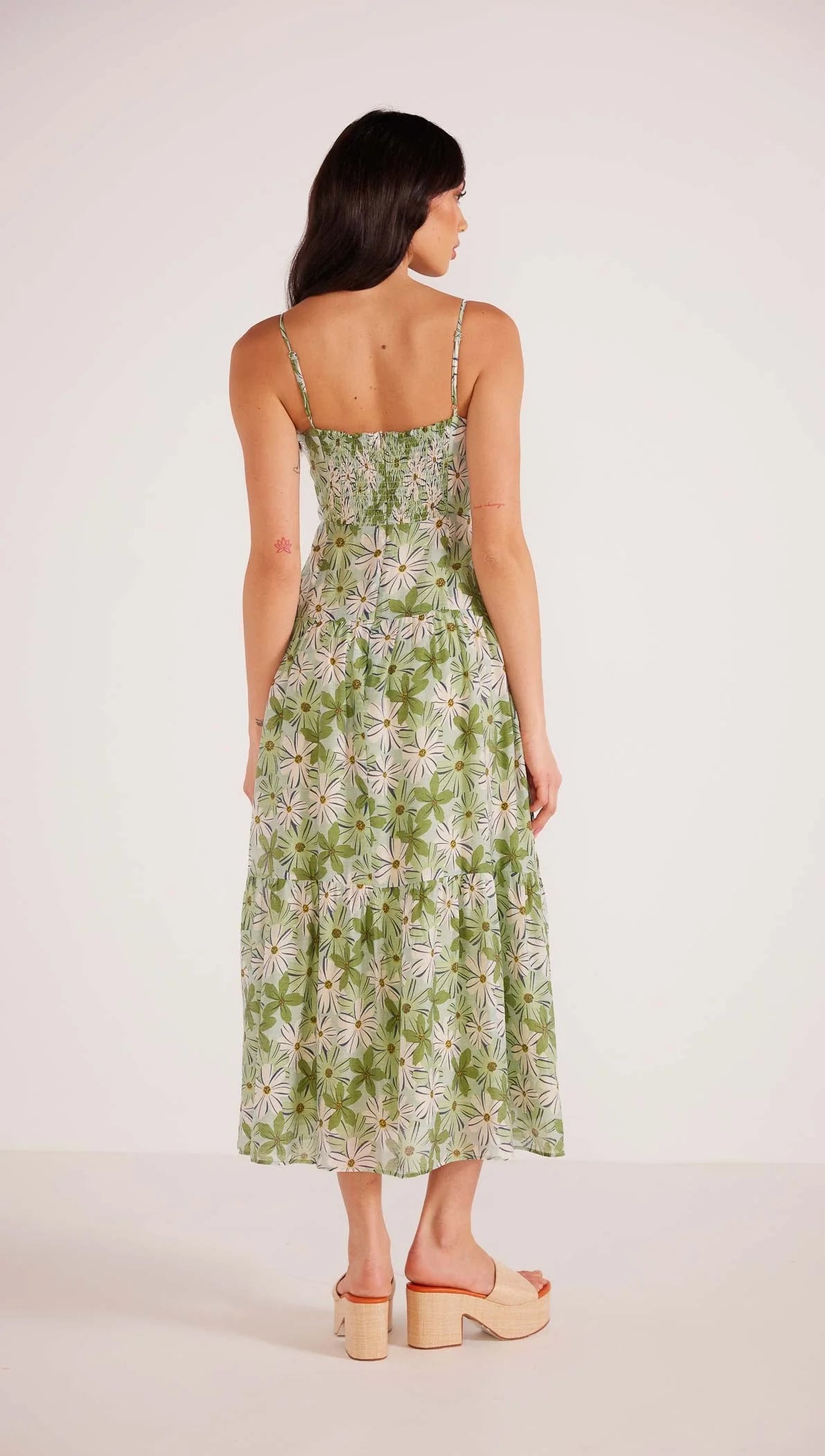 Back view of woman wearing a green and white floral print maxi dress with spaghetti straps and a fit and flare silhouette