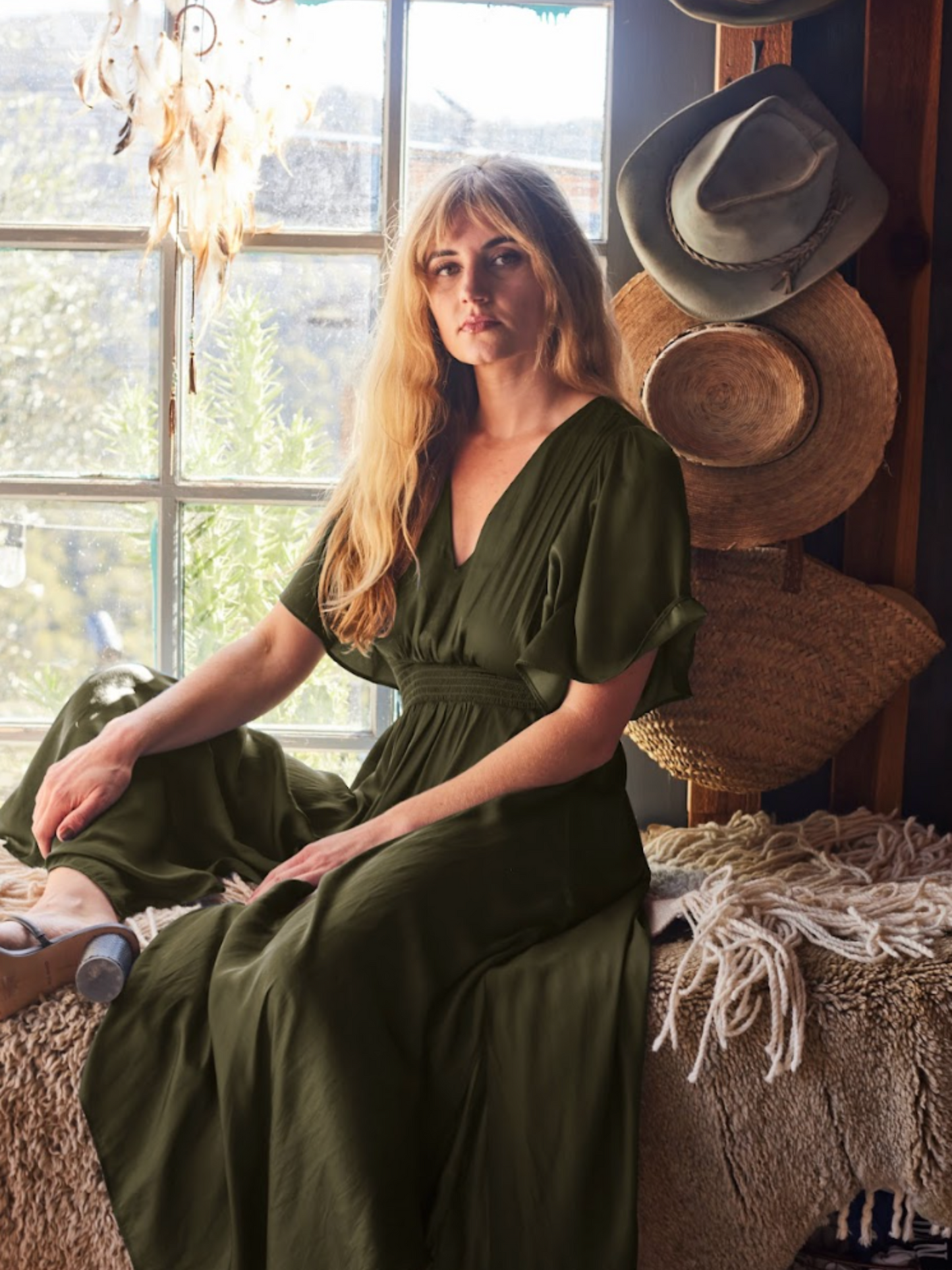 Woman sitting near a window wearing the green flutter sleeve Diana Dress by Harbour Thread