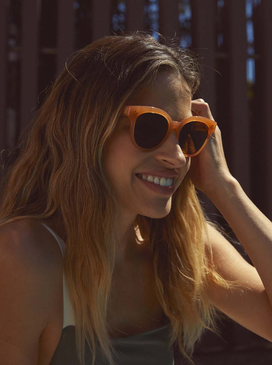 Woman wearing RAEN's Nikol Women's Cat-Eye Sunglasses with Papaya frame and Vibrant Brown Polarized lenses