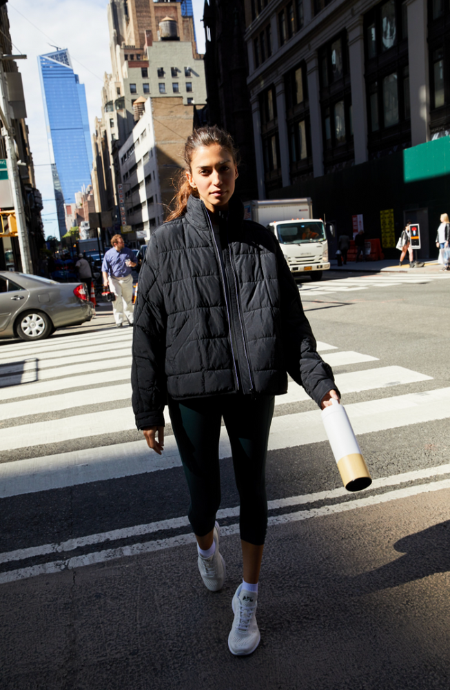 A woman walking down a city street while wearing the Pippa Packable Black Puffer Jacket by Free People