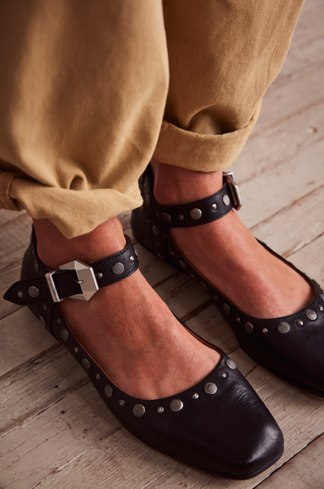 
                      
                        Black studded flats from Free People worn with beige pants on a wooden floor
                      
                    