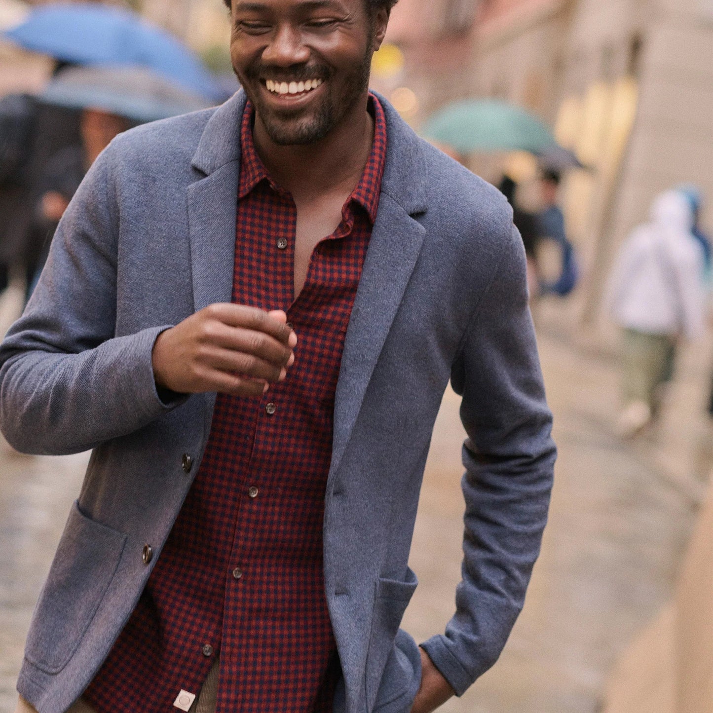 Man wearing a blue blazer over a red plaid shirt on a street.