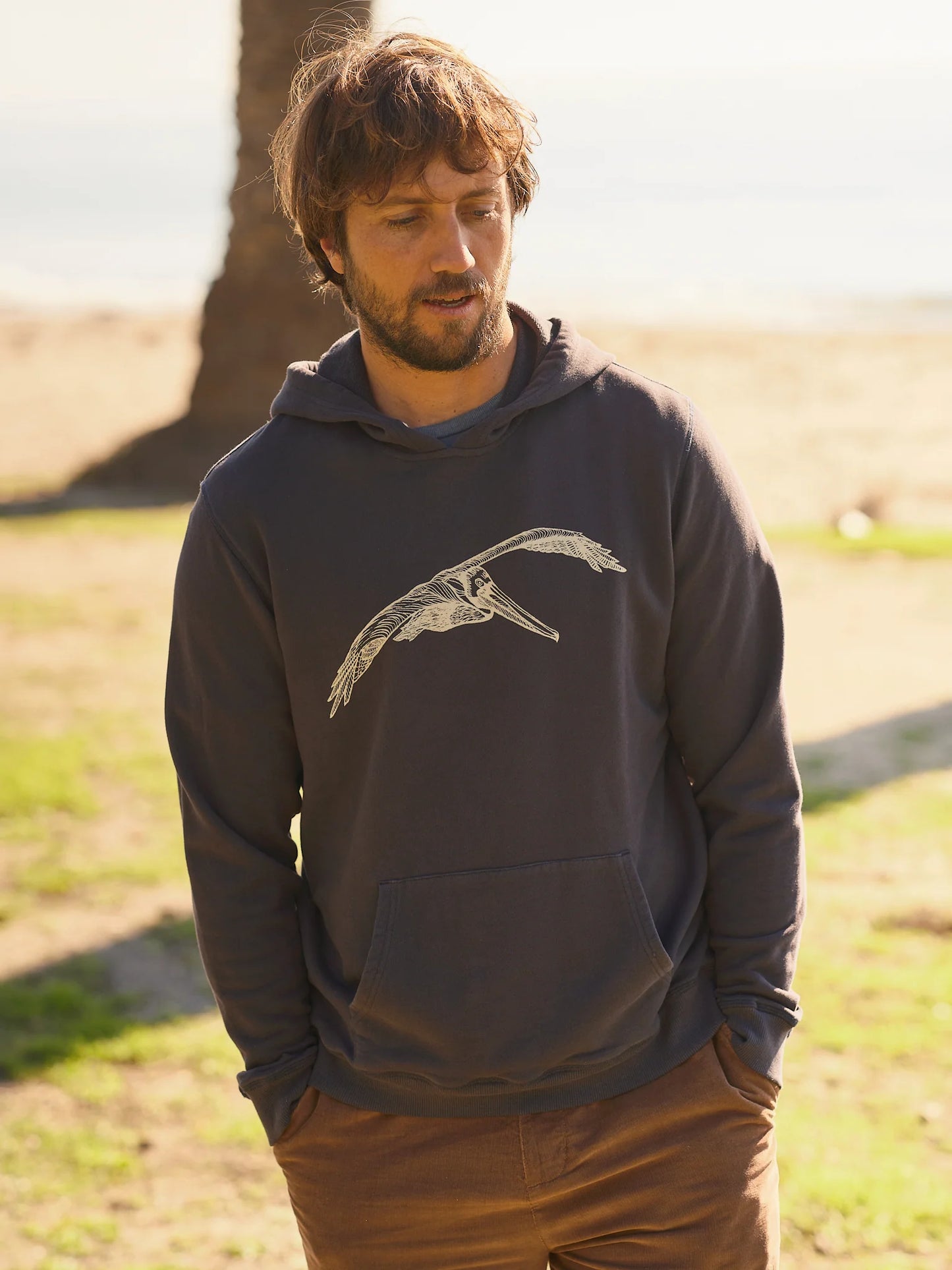 Front view of man wearing a faded navy hooded pullover with a pelican graphic on the front