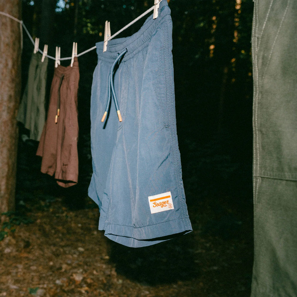 
                      
                        The Navy Yuma Light Shorts by the brand Seager hanging on a clothes line outdoors along with other pairs of shorts
                      
                    