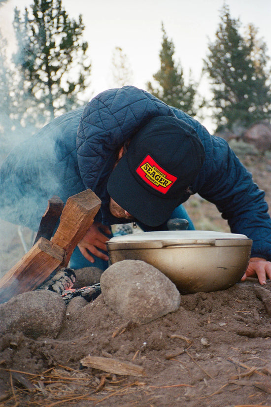 Man making a campfire while wearing the Black Ranahan Snapback Hat by Seager