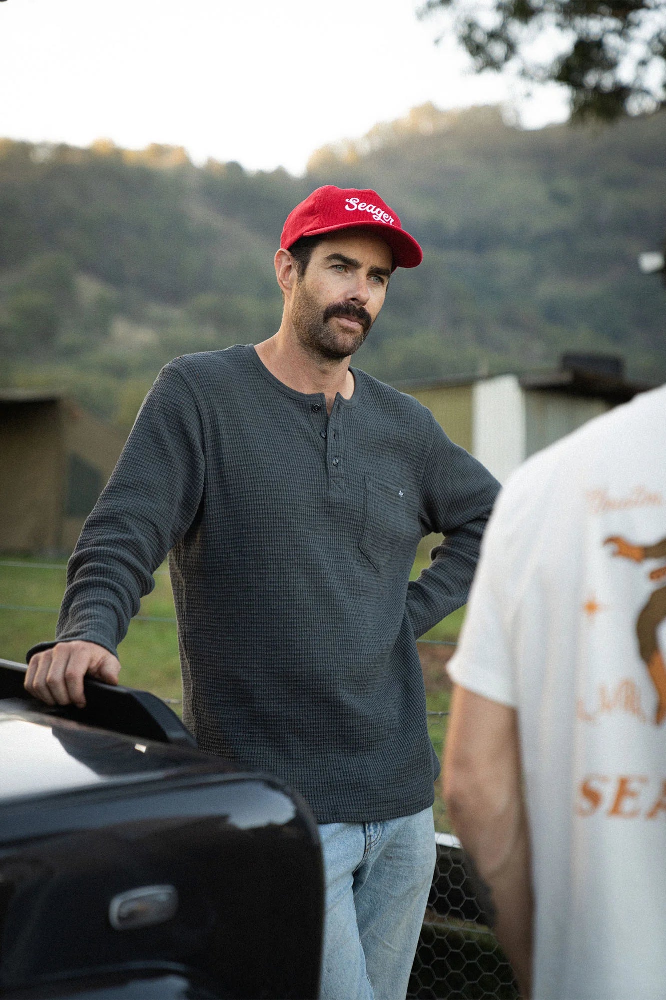 A man standing outside talking while wearing the Vintage Black Sawpit Henley Long Sleeve Thermal by Seager