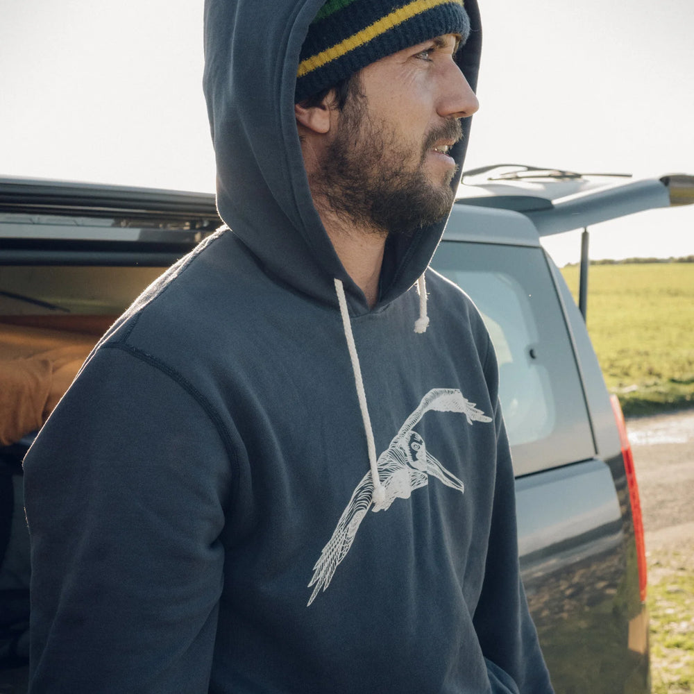 Side view of man wearing a faded navy hooded pullover with a pelican graphic on the front