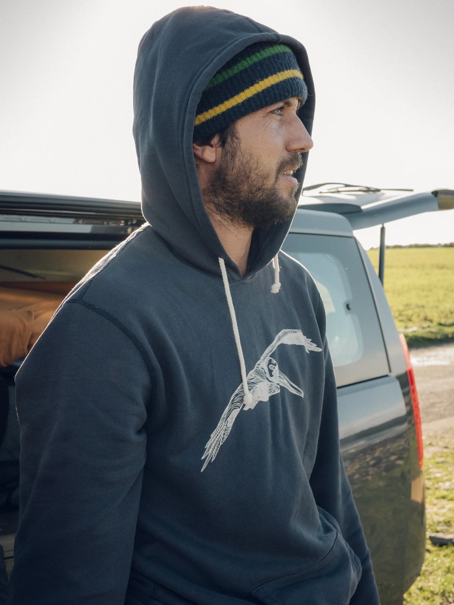 Side view of man wearing a faded navy hooded pullover with a pelican graphic on the front