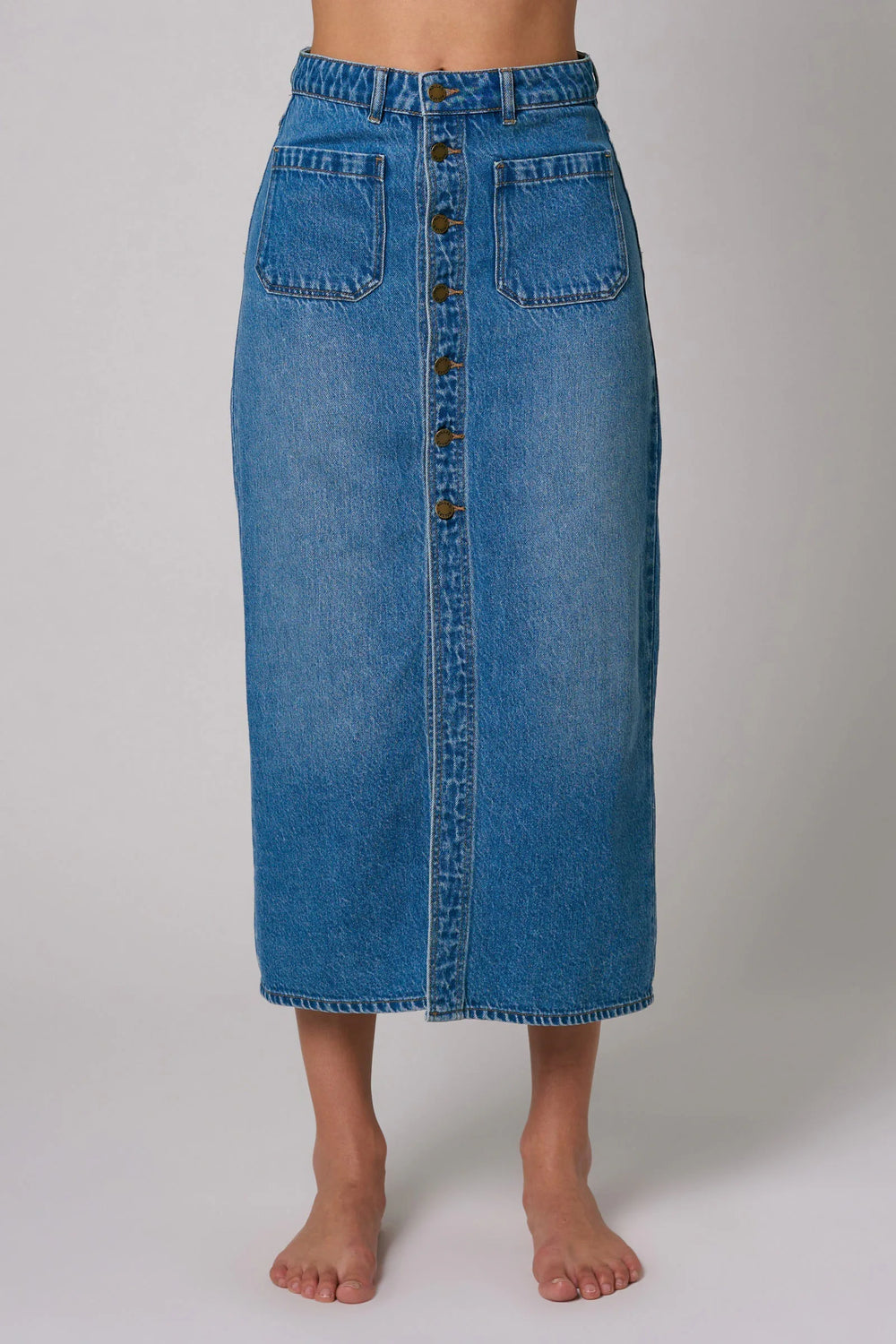 Front view of a medium wash denim midi skirt with front button closure and 2 patch pockets