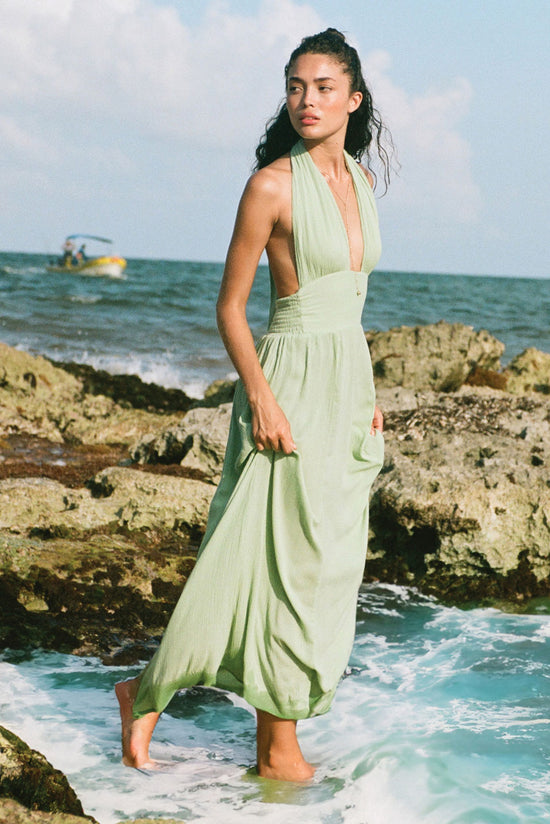 Load image into Gallery viewer, Lifestyle image of woman at the beach wearing a sage green color multi-wear wrap tie maxi dress
