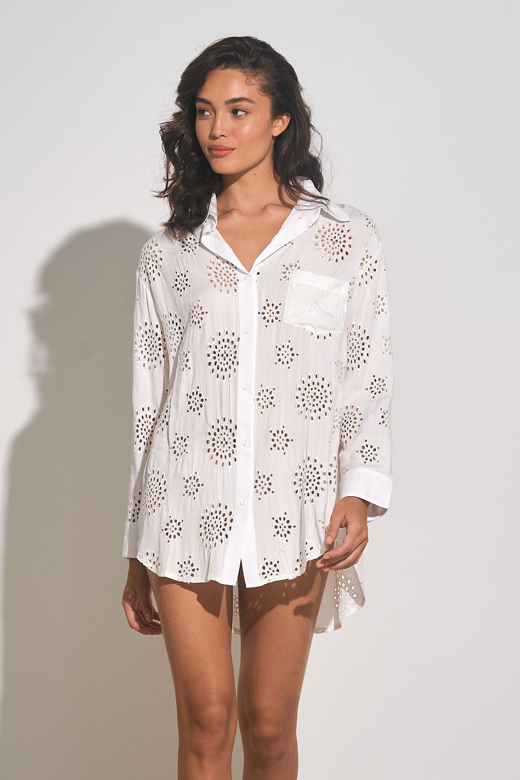 Front view of woman wearing a white long sleeve button down cover up shirt with eyelet embroidery throughout