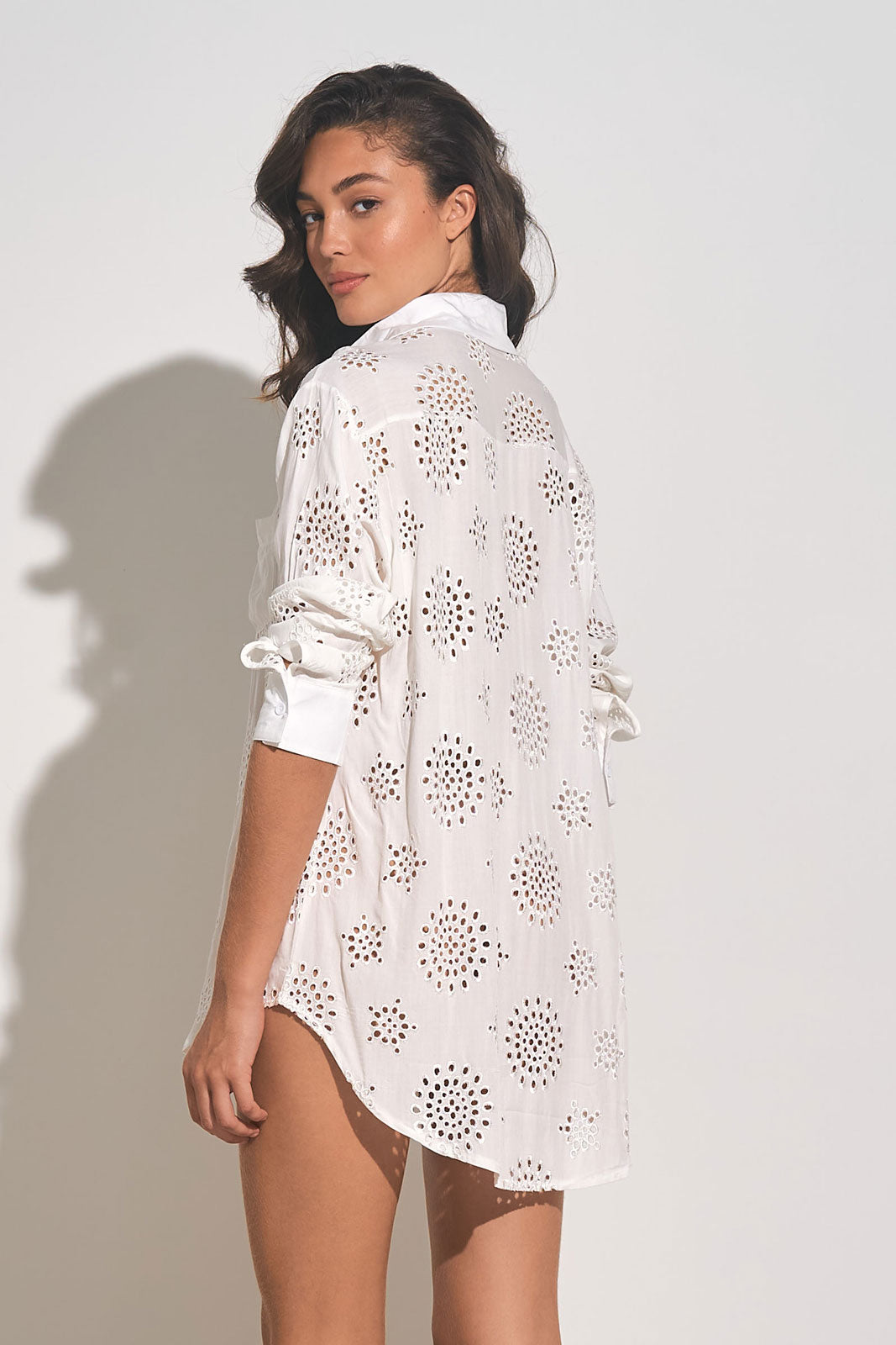 back view of woman wearing a white long sleeve button down cover up shirt with eyelet embroidery throughout