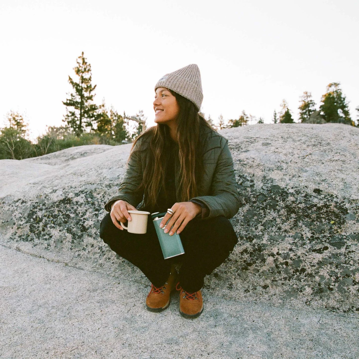 A woman by a rock while camping. She's wearing the Base Camp Jacket by the brand Roark