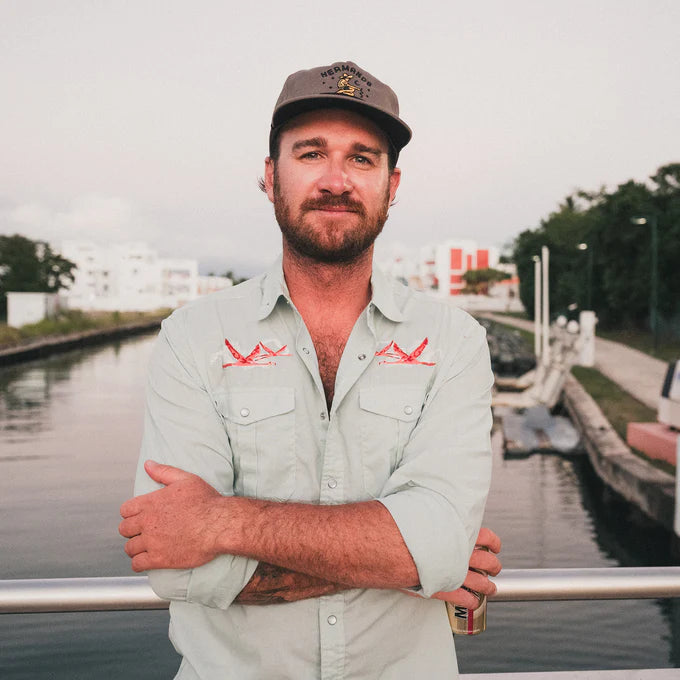 Outdoor lifestyle photo of man wearing a light blue long sleeve snap button up shirt with flamingo embroidery at the chest