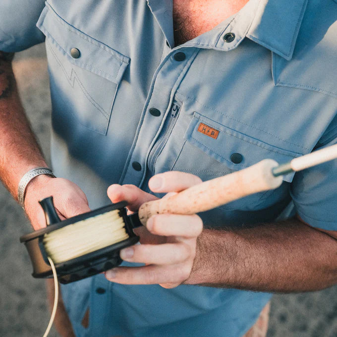 Man wearing the Howler Bros Emerger Tech Shirt in the color Berges Blue