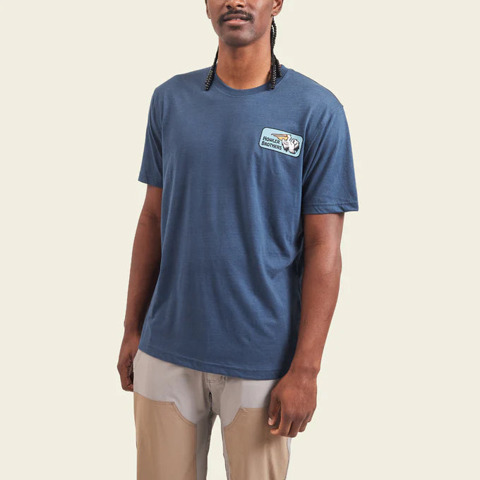 Front view of man wearing the blue Pelican Badge short sleeve t-shirt by Howler Bros