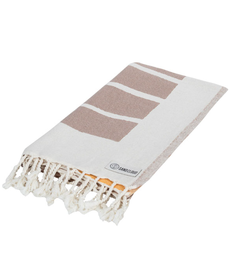 folded view of a sand cloud beach towel with a sun and sea inspired design and tassels at the ends