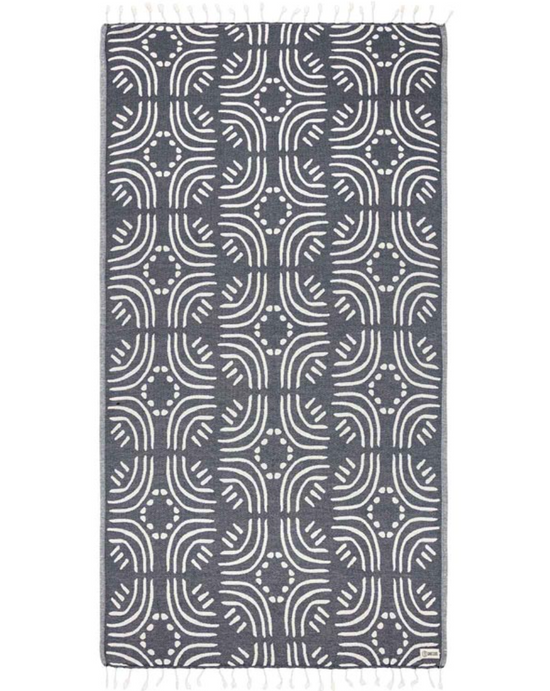 Unfolded view of a navy beach towel with white line and dot design throughout and tassels at the ends