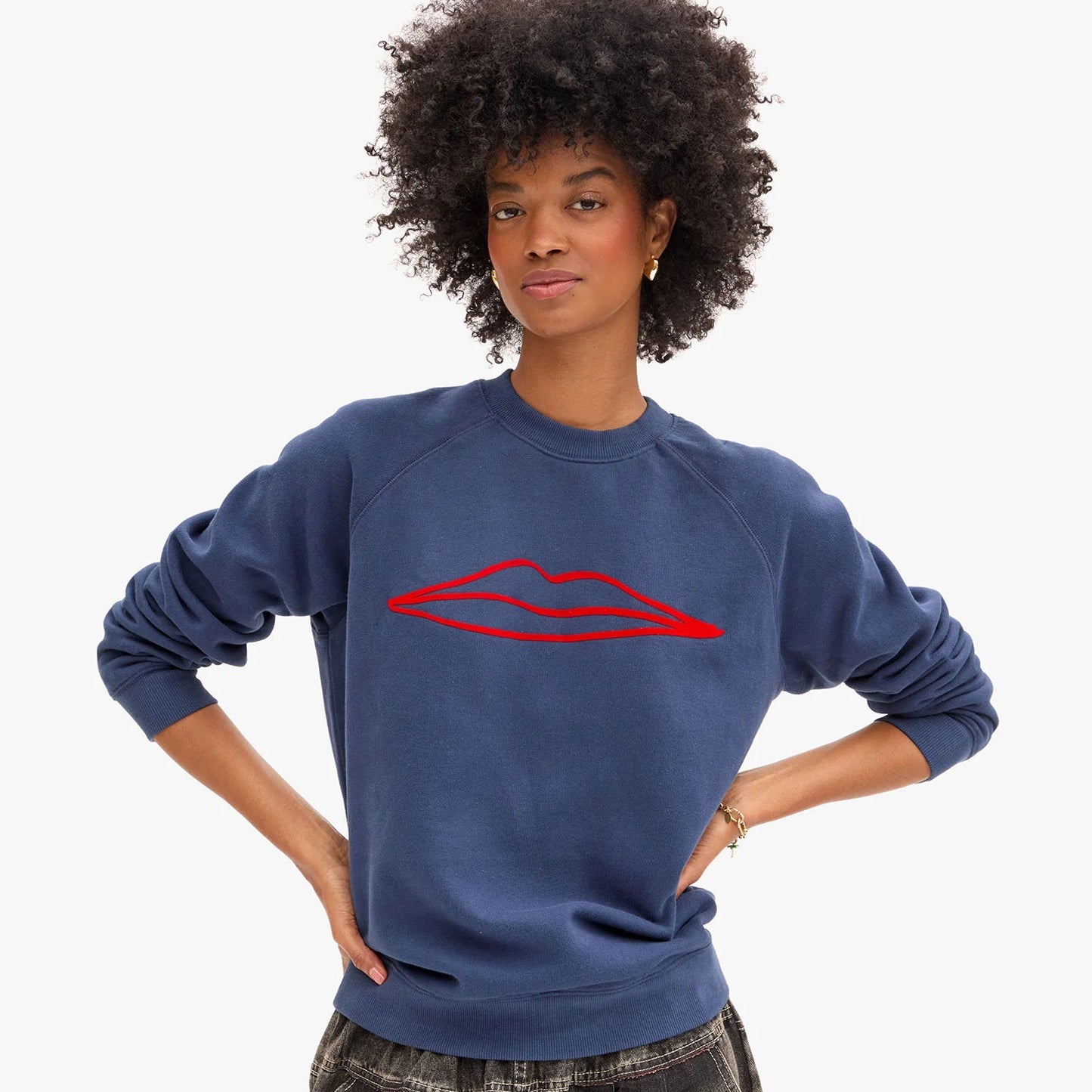 Woman wearing a navy blue sweatshirt  from Clare V. with a red lips graphic design on the front