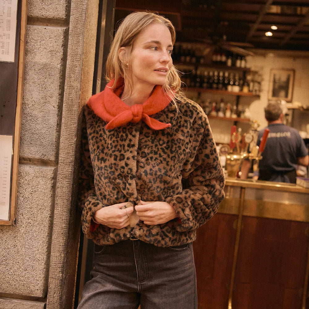 A woman wearing the Marine Layer Tessa Leopard Jacket with an orange scarf