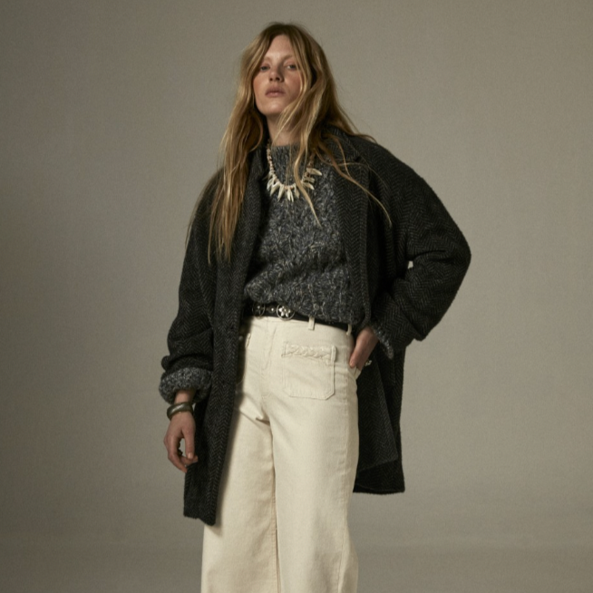 Woman wearing a sweater and white trousers layered under the Maison Hotel Marceau Jacket