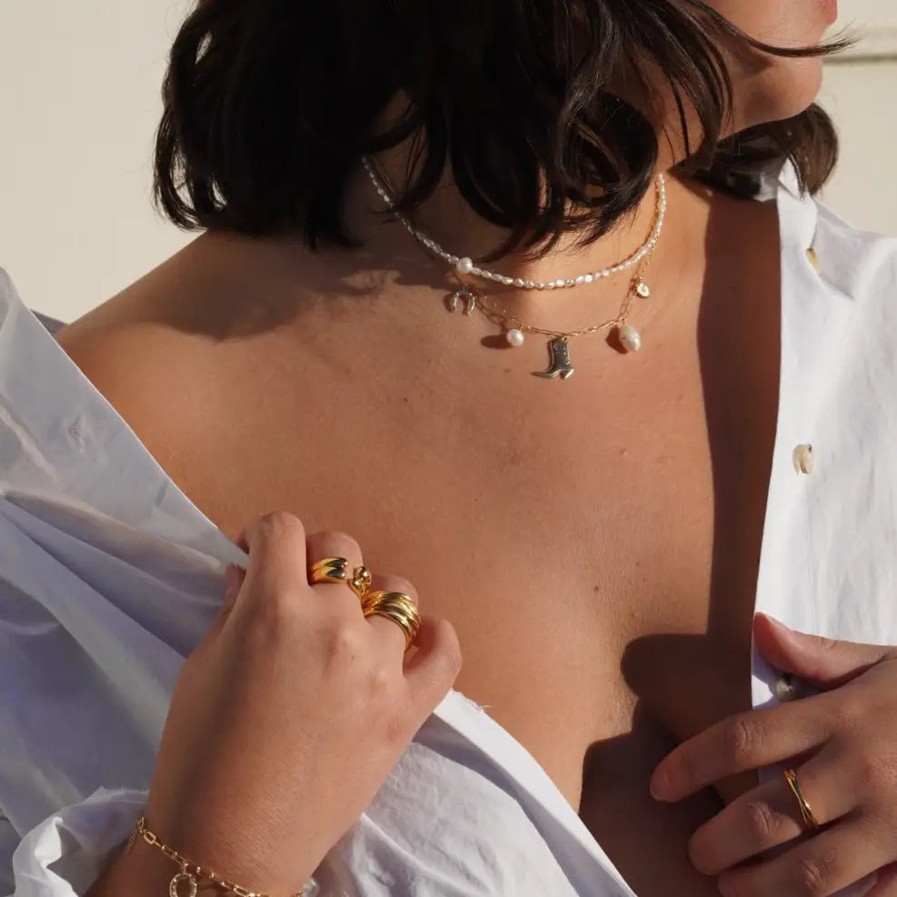 A woman wearing the Sea Ranch Charm Necklace by May Martin layered with a pearl choker