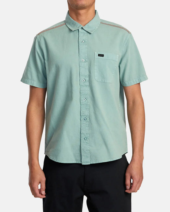 Front view of man wearing a green color short sleeve button up shirt by RVCA