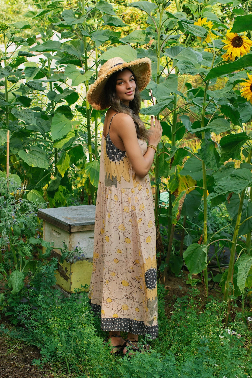 A woman standing near flowers while wearing the Milk & Honey Bohéme Slip Dress by Market of Stars