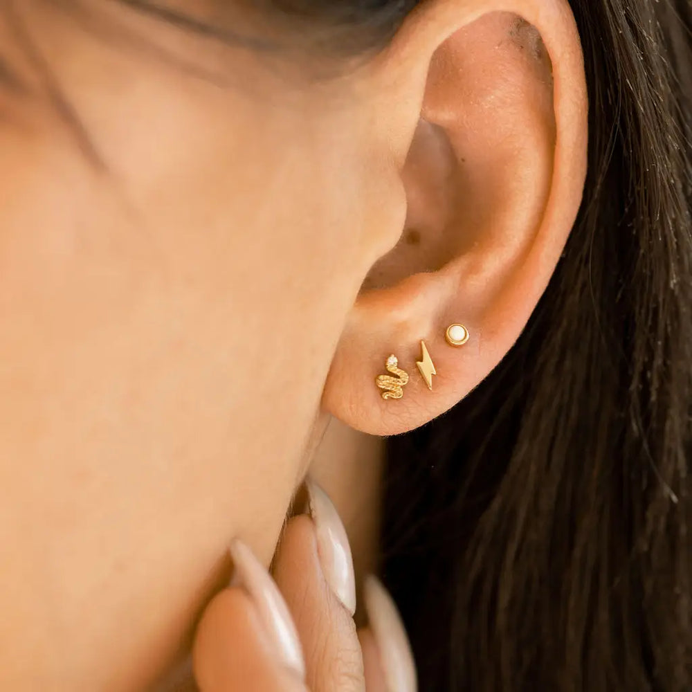 
                      
                        A woman wearing the Gold Snake Stud Earrings by The Land Of Salt along with other studs
                      
                    