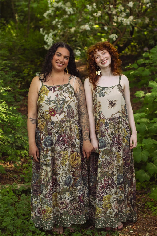 
                      
                        Two women wearing floral dresses standing in a forest setting.
                      
                    