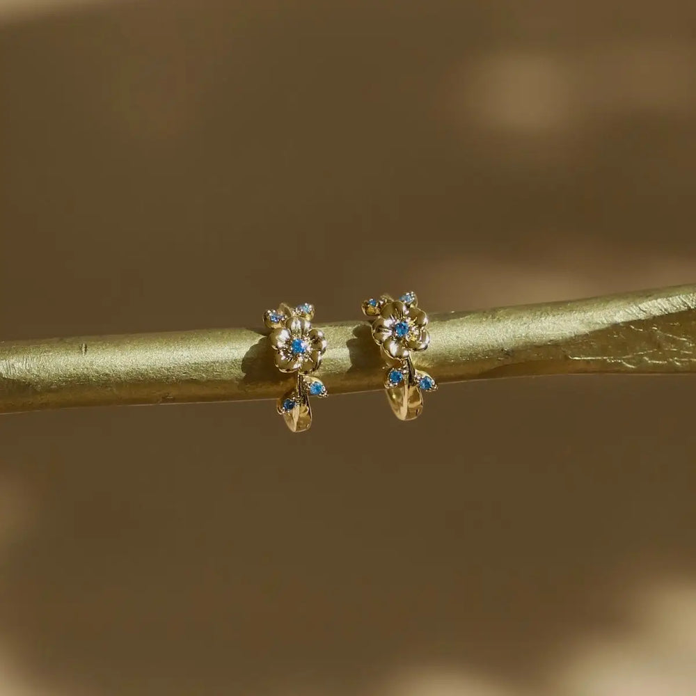 Gold earrings with blue stones on a branch against a blurred natural background