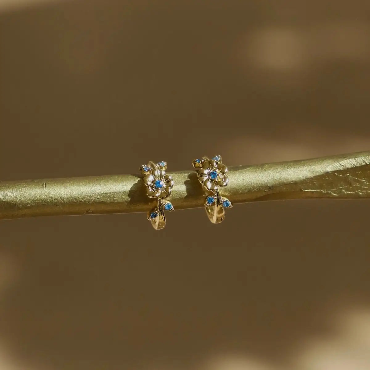 Gold earrings with blue stones on a branch against a blurred natural background