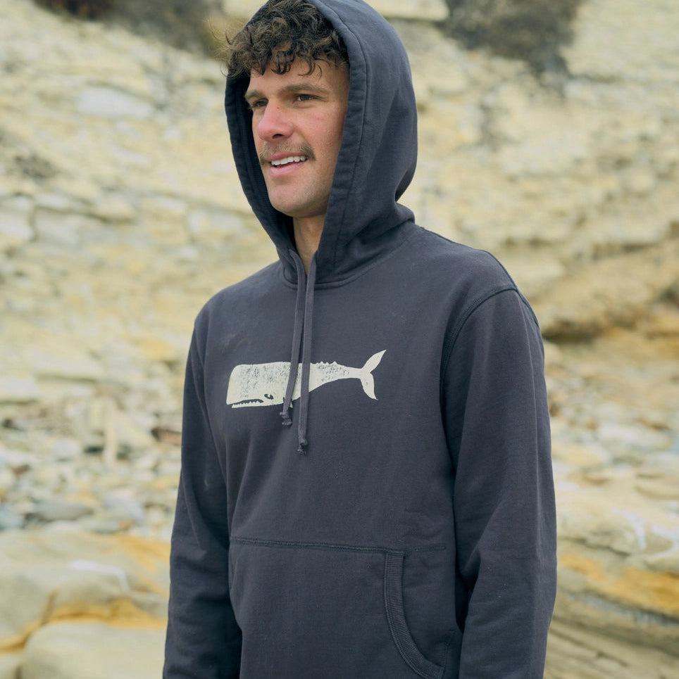 Man wearing the Max Whale Pullover from Mollusk on a rocky beach 