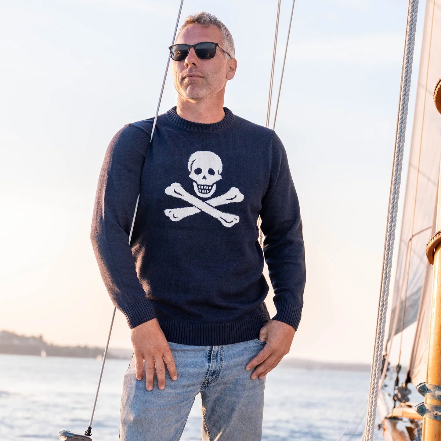 A man wearing the navy  Bellamy SeaWell Sweater from Long Wharf Supply while standing on a boat