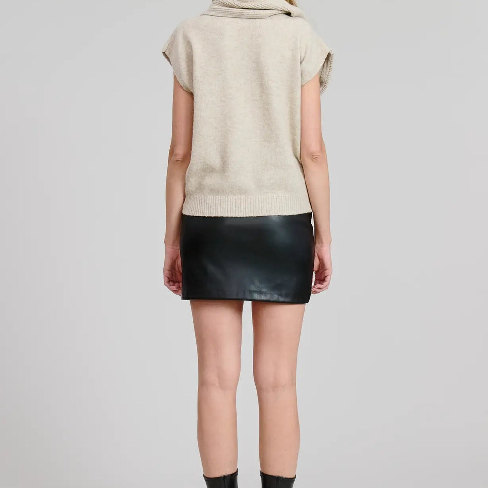 
                      
                        Person wearing a beige short sleeve sweater top with attached scarf detail, black leather skirt, and black boots
                      
                    