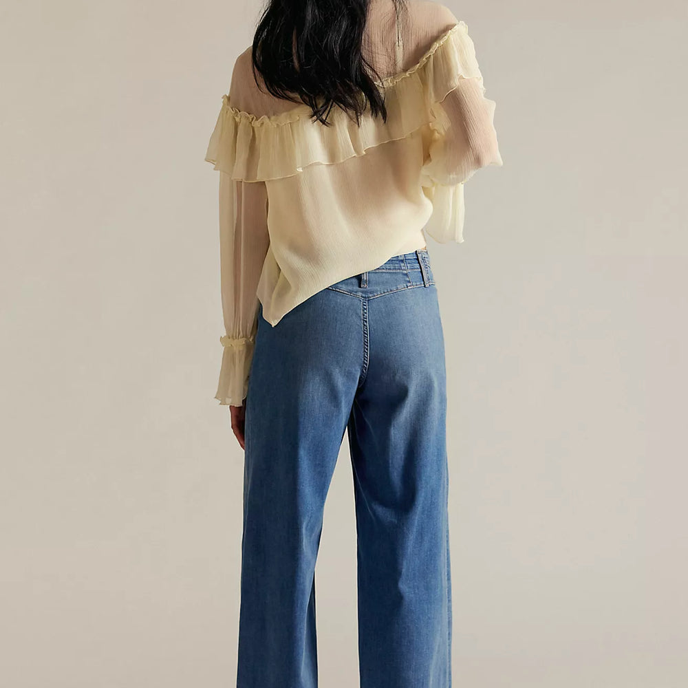 
                      
                        Person wearing a light yellow blouse with ruffled sleeves and blue jeans on a beige background
                      
                    