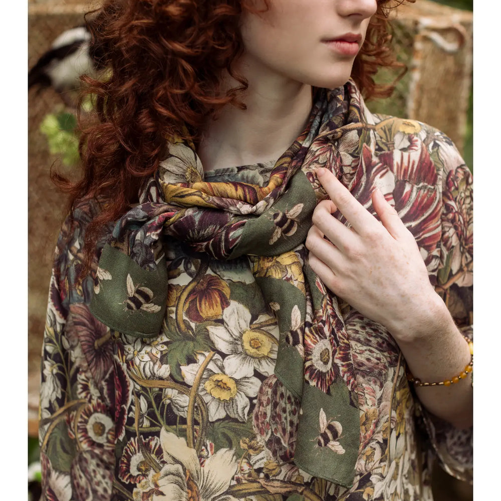 
                      
                        A woman wearing the Love Grows Wild Floral Bamboo Scarf with Bees by Market of Stars around her neck as a scarf
                      
                    