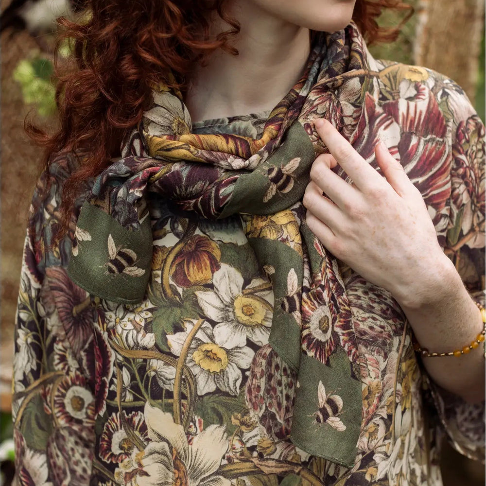 A woman wearing the Love Grows Wild Floral Bamboo Scarf with Bees by Market of Stars around her neck as a scarf