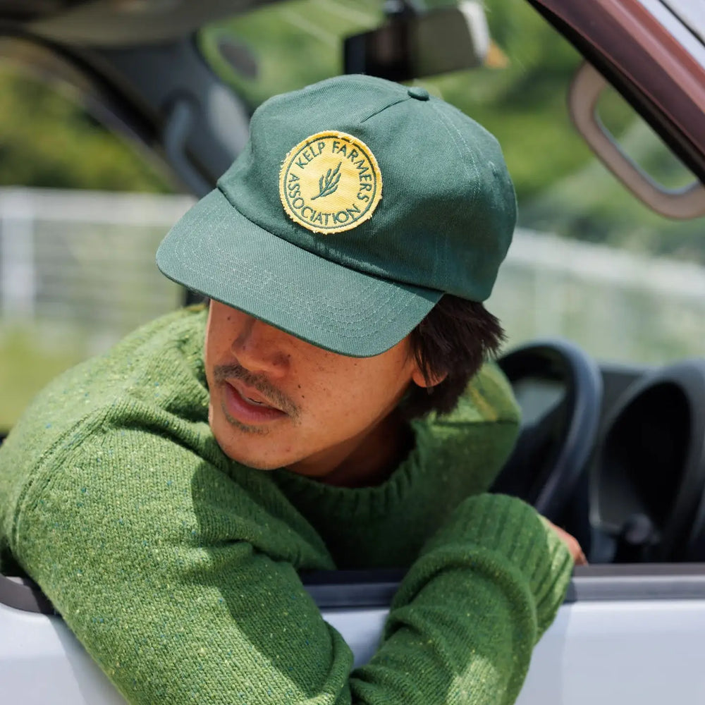 Person wearing a green cap and sweater, sitting inside a vehicle.