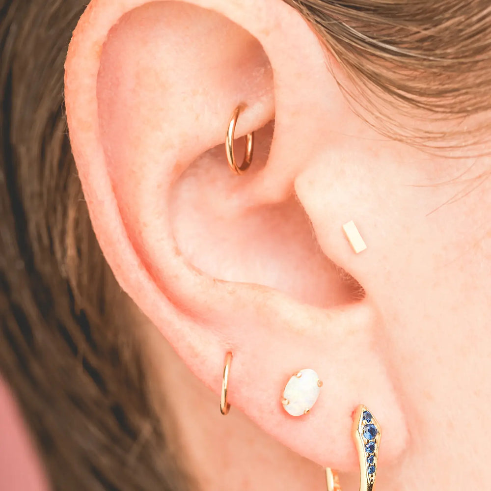 A person wearing the Gold Viper Sapphire Hoop Earrings by Mineral and Matter along with other earrings